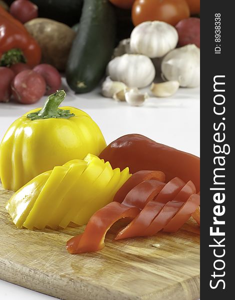 Fresh sliced peppers on wooden background with vegetables on the background