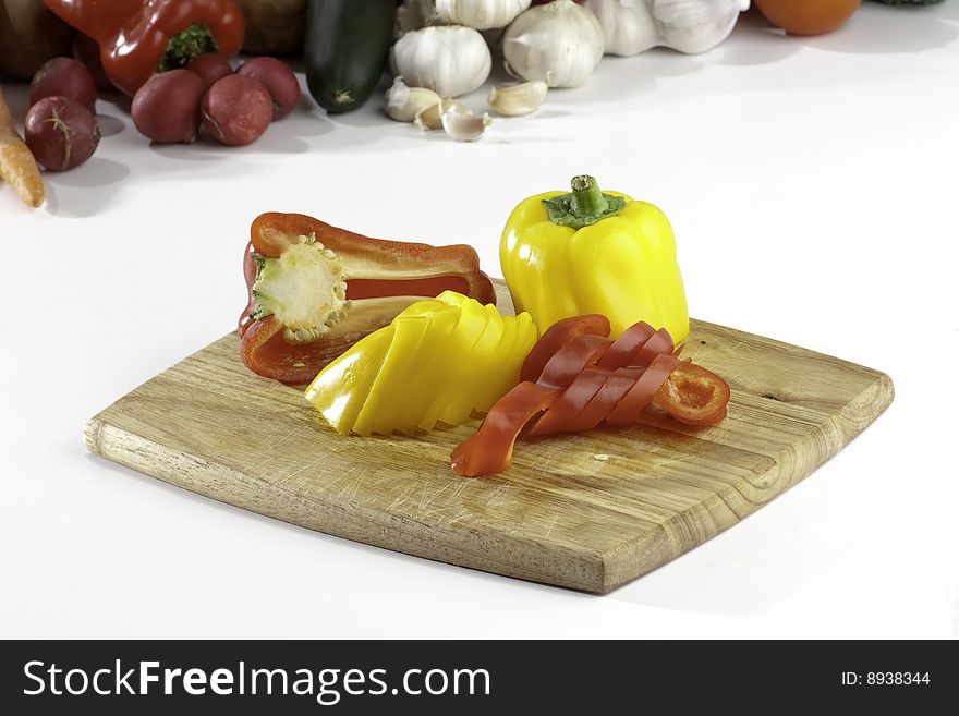 Fresh sliced peppers on wooden background with vegetables on the background