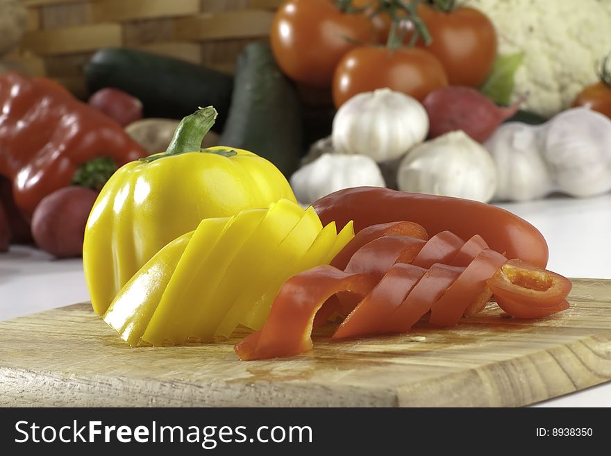 Fresh sliced peppers on wooden background with vegetables on the background