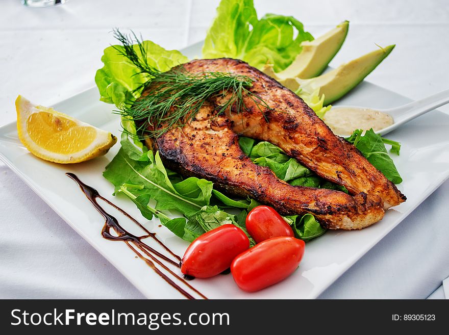 A fried fish medallion on a bed of green salad with avocado and tomatoes. A fried fish medallion on a bed of green salad with avocado and tomatoes.