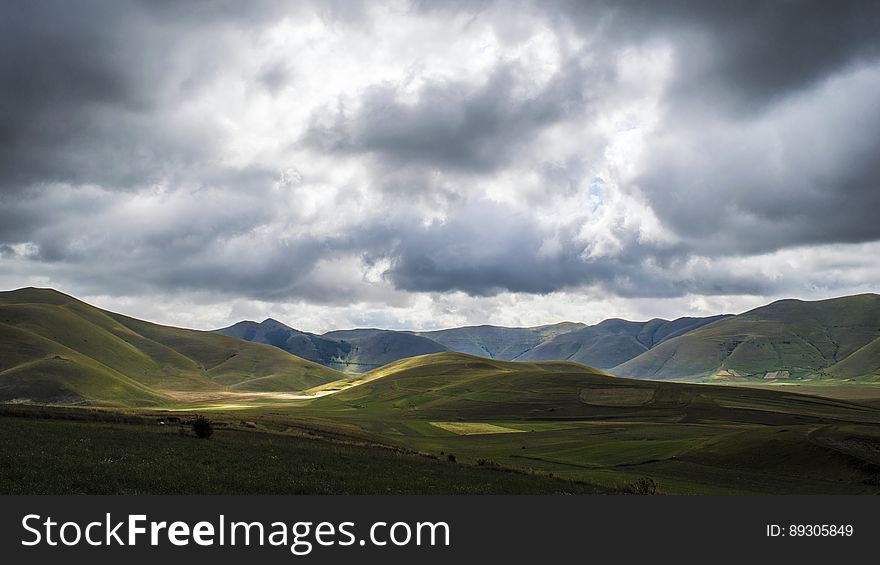 A landscape with green hills and dark clouds.