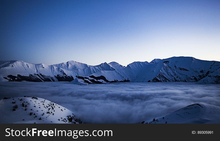 A mountain valley in fog and snowcapped peaks in the background.