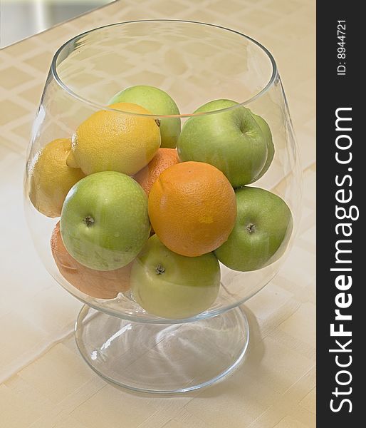 Oranges, apples, lemons in the big glass on a table. Oranges, apples, lemons in the big glass on a table