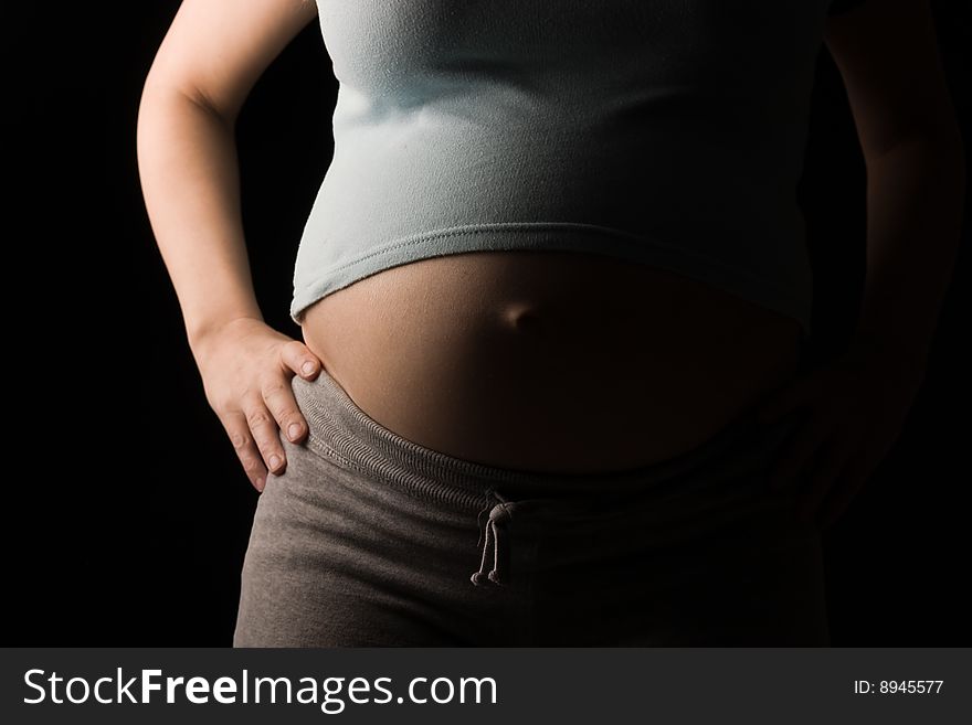 Pregnant woman's abdomen side lit on black. Pregnant woman's abdomen side lit on black