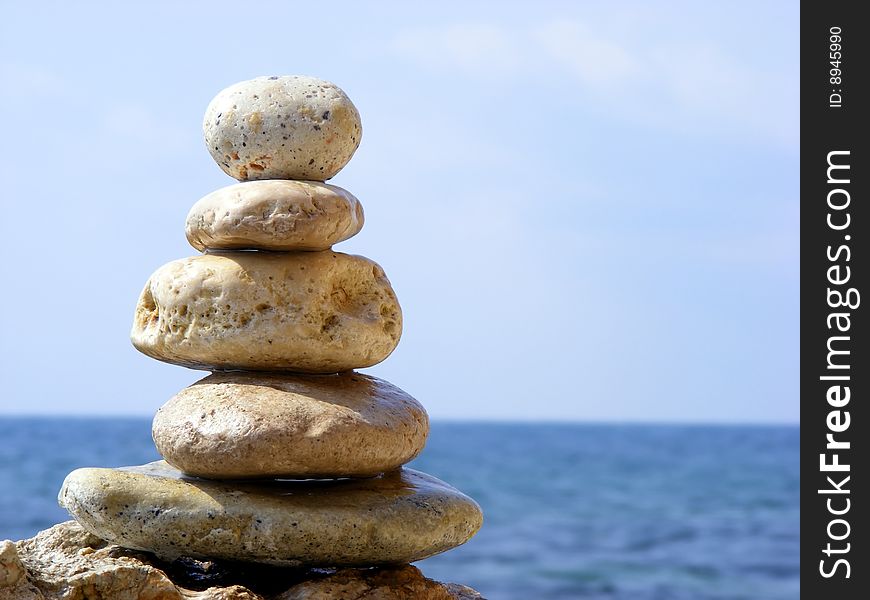 The pyramid of stones on a background of sea and sky with the horizon line in the sun clear cloudless day. The pyramid of stones on a background of sea and sky with the horizon line in the sun clear cloudless day