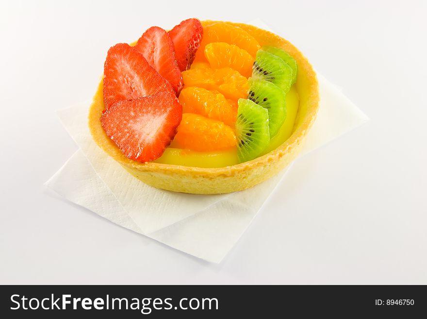 Strawberry, mandarin and kiwi custard fruit tart on a napkin with a white background