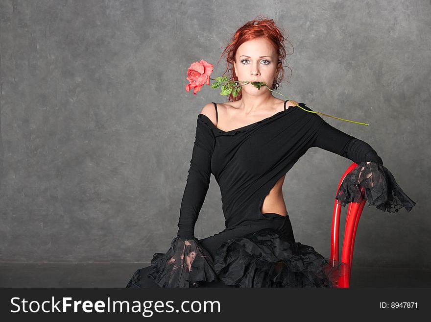 The charming girl with a red rose on a chair