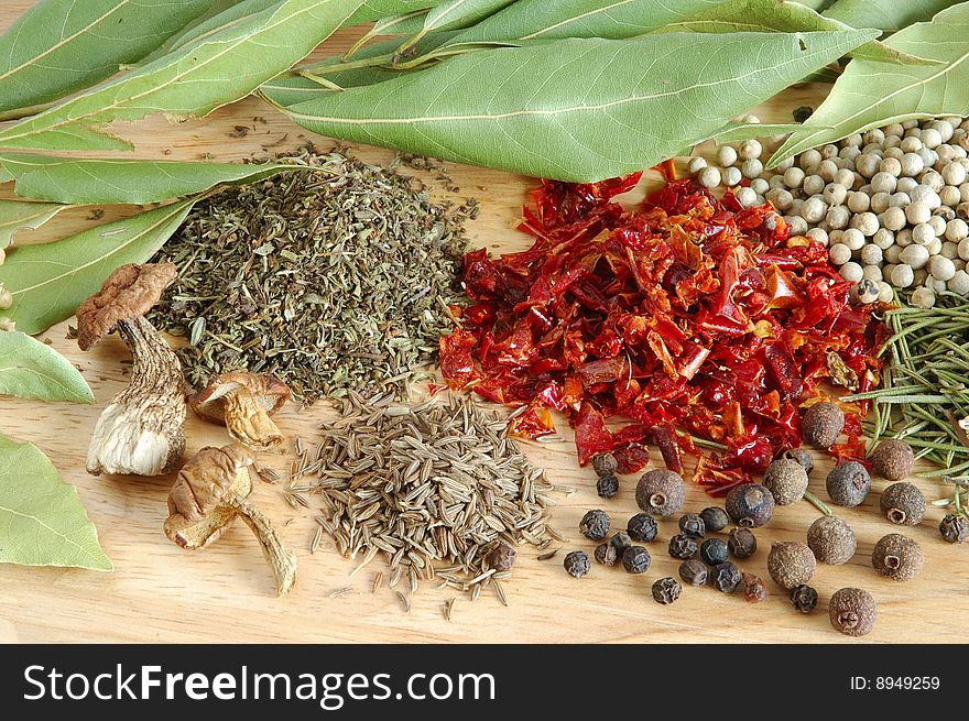 Piles of spices on wooden background. Fresh bay leaves, whole black and white pepper, coriander, rosemary, caraway-seeds, dry paprika and dry porcini mushrooms.