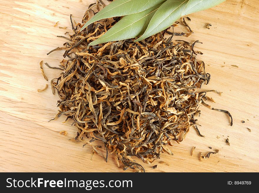 Aromatic dry yellow tea and fresh leaves on wooden board