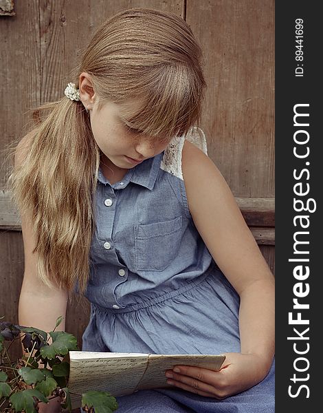 Portrait of young girl in blue dress sitting outdoors in garden reading on sunny day. Portrait of young girl in blue dress sitting outdoors in garden reading on sunny day.