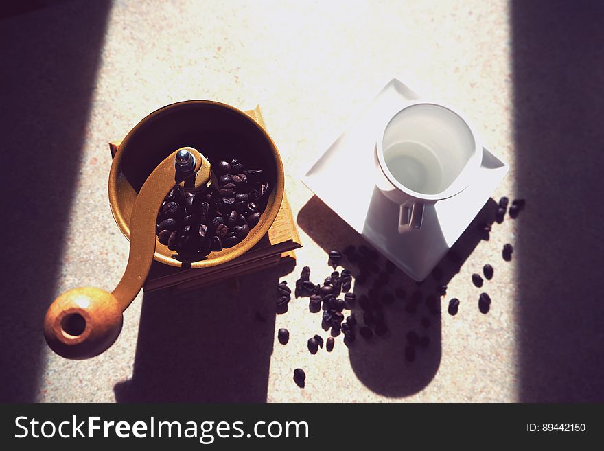 Coffee mill with whole beans next to empty white china cup and sauce in sunlight. Coffee mill with whole beans next to empty white china cup and sauce in sunlight.