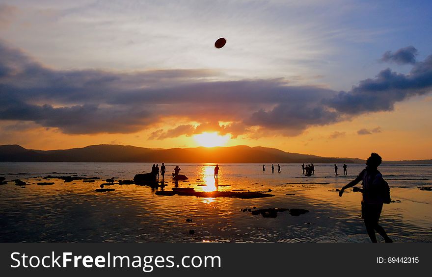 People Playing On Beach At Sunset