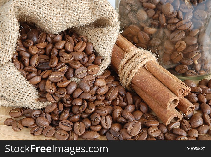 Coffee beans and cinnamon sticks in canvas sack on wooden background. Coffee beans and cinnamon sticks in canvas sack on wooden background