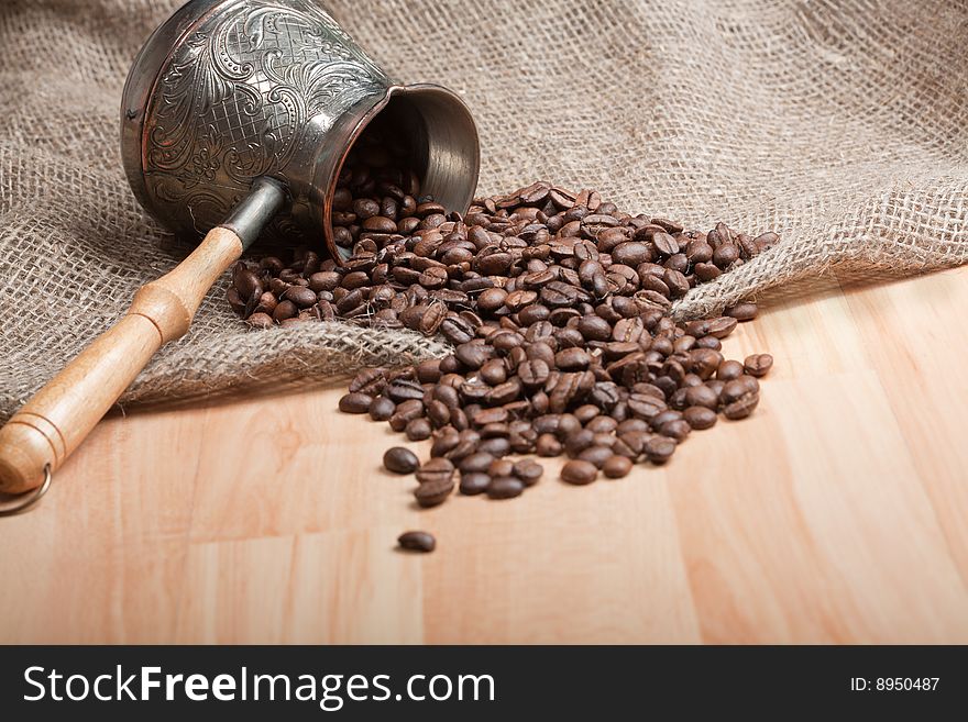 Sackcloth bag with cezve and roasted coffee beans on table