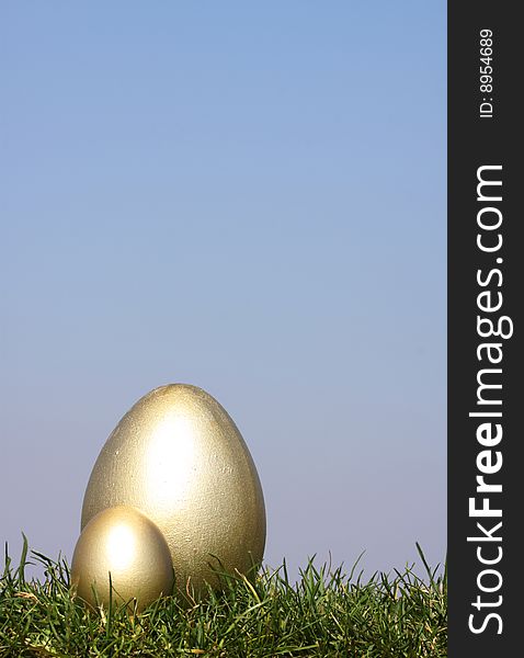 2 Gold Easter eggs in grass against  a bright blue sky