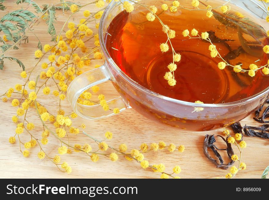 Glass cup with tea and blooming yellow mimosa on wooden background. Glass cup with tea and blooming yellow mimosa on wooden background