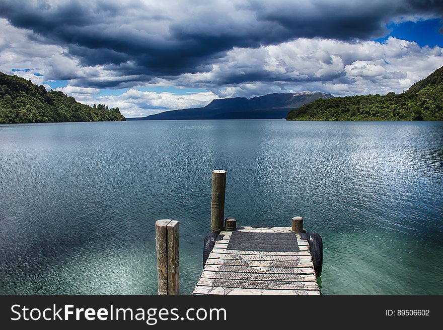 Empty wooden dock along shoreline of lake with cloudy skies. Empty wooden dock along shoreline of lake with cloudy skies.