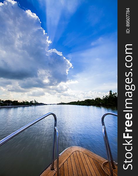 Wooden deck of yacht on blue waters of river against blue skies with white clouds.