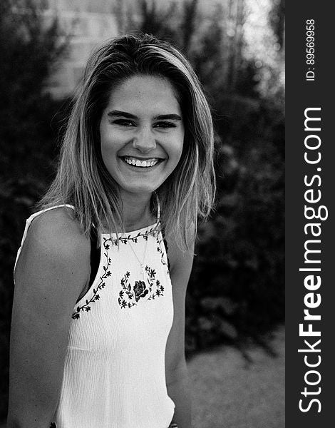 Portrait of young woman with long blond hair wearing white top smiling outdoors in black and white. Portrait of young woman with long blond hair wearing white top smiling outdoors in black and white.