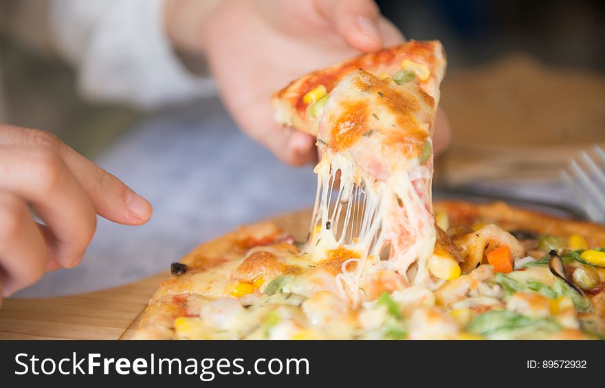 Hands lifting piece of cheesy vegetable pizza from wooden board. Hands lifting piece of cheesy vegetable pizza from wooden board.