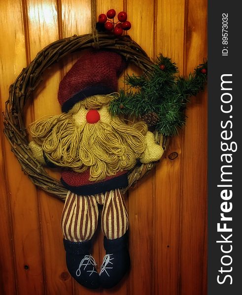 Christmas wreath with pine bow and cloth Santa Claus hanging on wooden planks. Christmas wreath with pine bow and cloth Santa Claus hanging on wooden planks.