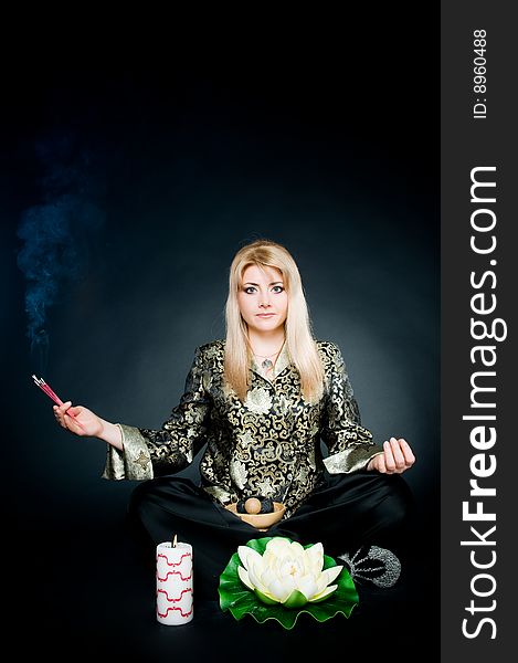 Woman relaxing in lotus pose with aroma sticks, lotus, and candle