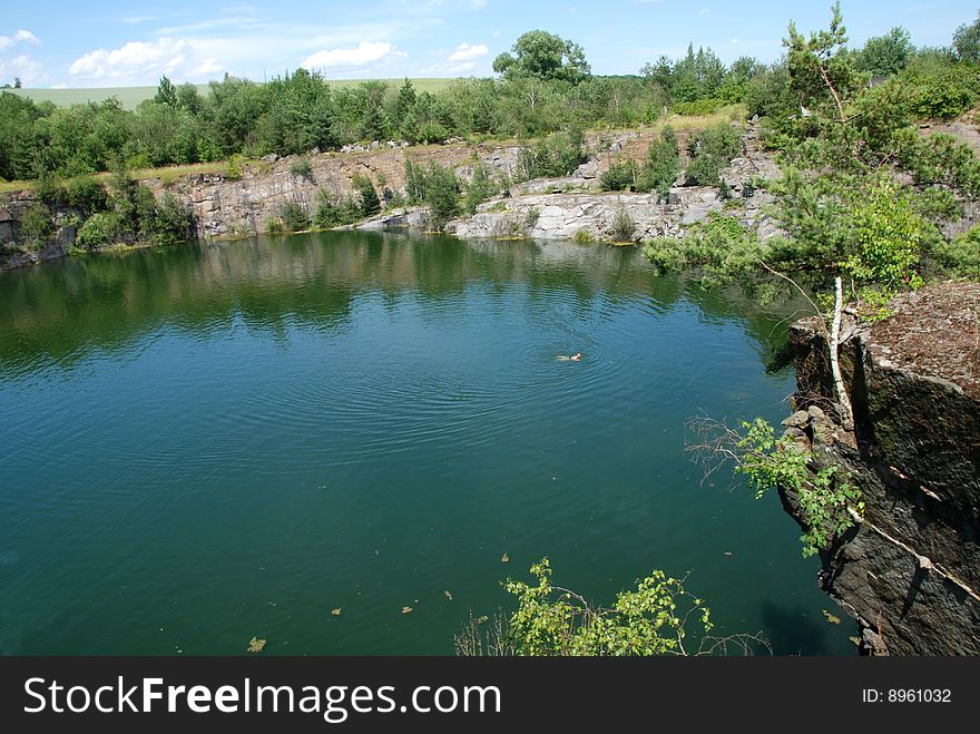 Old flooded quarry with calm water and growing trees