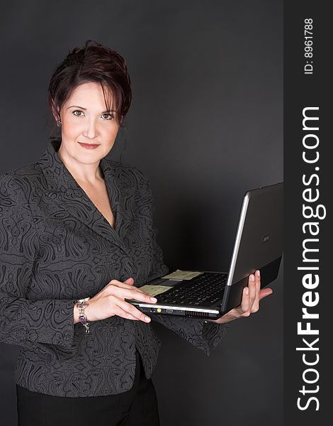 Composed Businesswoman holding a laptop against a black background. Composed Businesswoman holding a laptop against a black background