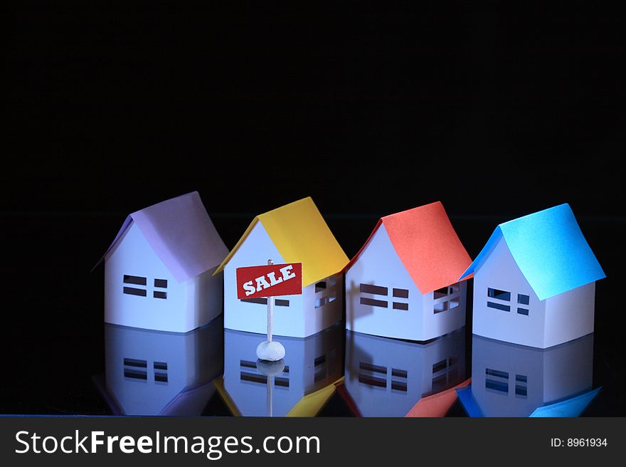 Few papery houses with colored roofs and sale tablet on dark background. Few papery houses with colored roofs and sale tablet on dark background
