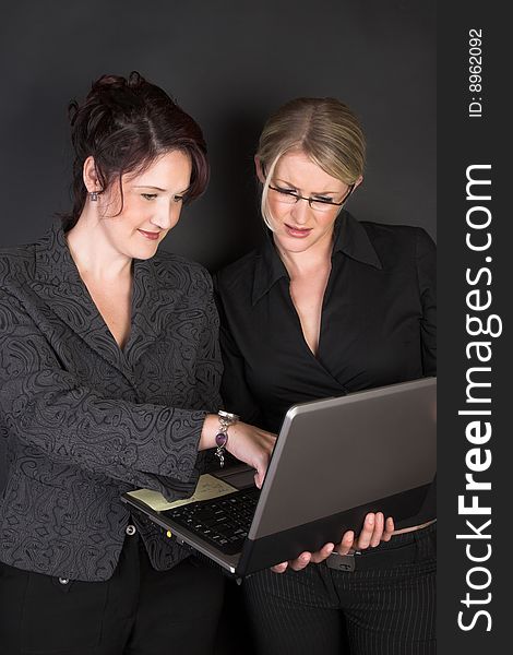 Composed Businesswomen holding a laptop against a black background. Composed Businesswomen holding a laptop against a black background