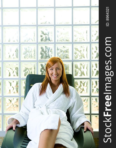 Young red-haired woman clothed bathrobe sitting on deckchair. She's smiling and looking at camera. Front view. Young red-haired woman clothed bathrobe sitting on deckchair. She's smiling and looking at camera. Front view.