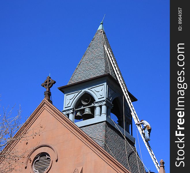 Worker descends ladder, after working on church spire. Worker descends ladder, after working on church spire.