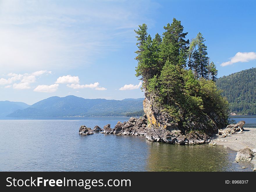 Small rocky cape with trees on mountain lake