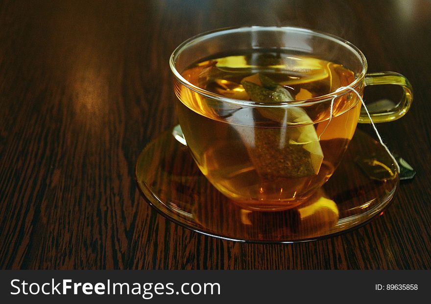 Close up of glass cup and sauce with tea bag and hot beverage on wooden tabletop. Close up of glass cup and sauce with tea bag and hot beverage on wooden tabletop.