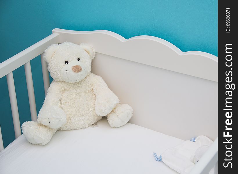 A cute white teddy bear in a crib. A cute white teddy bear in a crib.