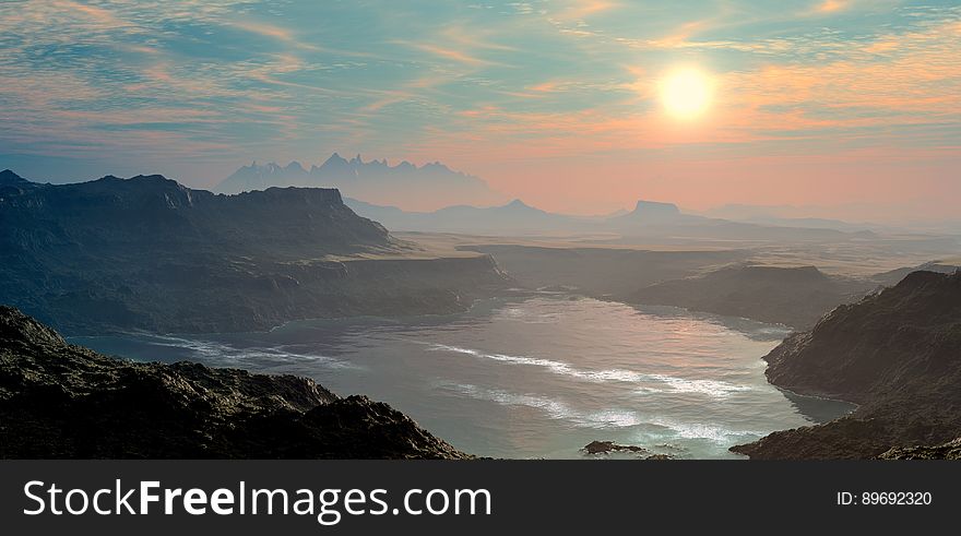 Sunset over rocky coastline with mountains on horizon.