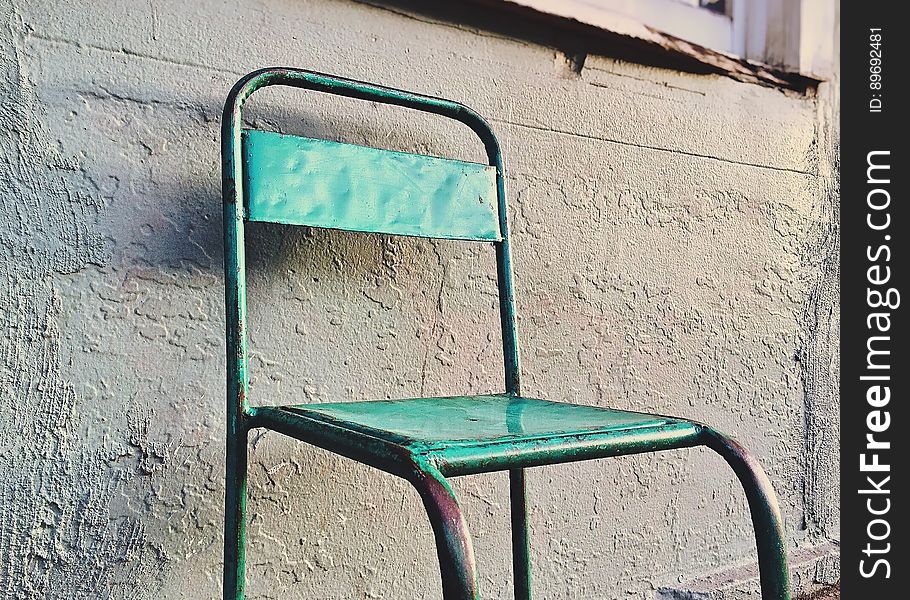Rusty green painted metal chair against concrete wall outdoors. Rusty green painted metal chair against concrete wall outdoors.