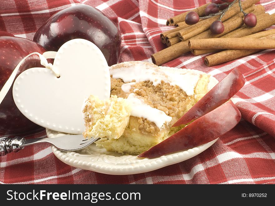 A piece of apple cinnamon streusel coffee cake on a plate with a bite of cake on a fork, with a blank heart shaped tag with copy space