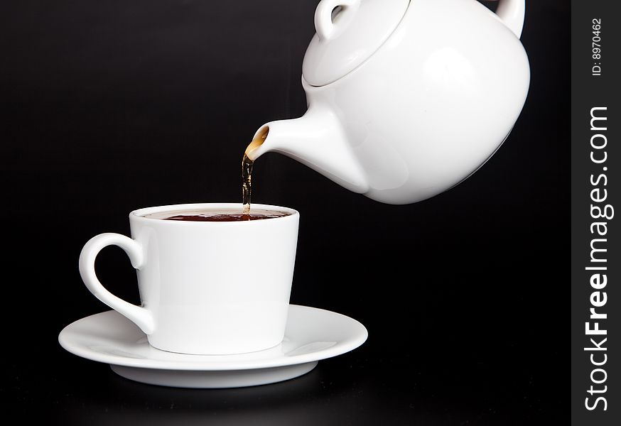 Pour tea from the teapot into the cup on a black background