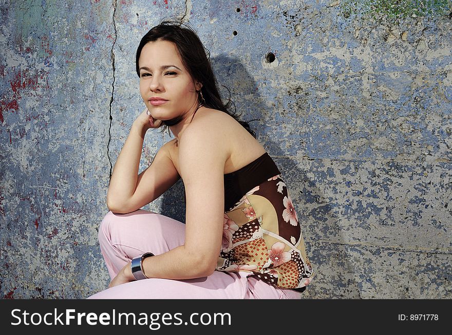 Portrait of young female fashion model sitting against grunge wall