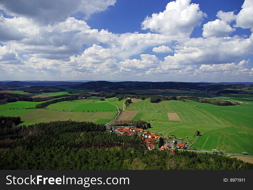 Rural landscape with green fields, village and blue sky