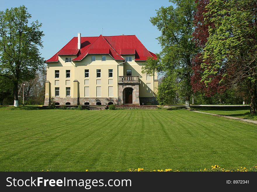 Old manor with red roof, green lawn foreward