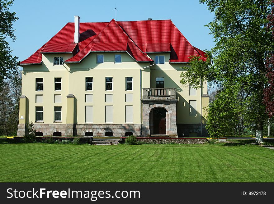 Old manor with red roof, green lawn foreward