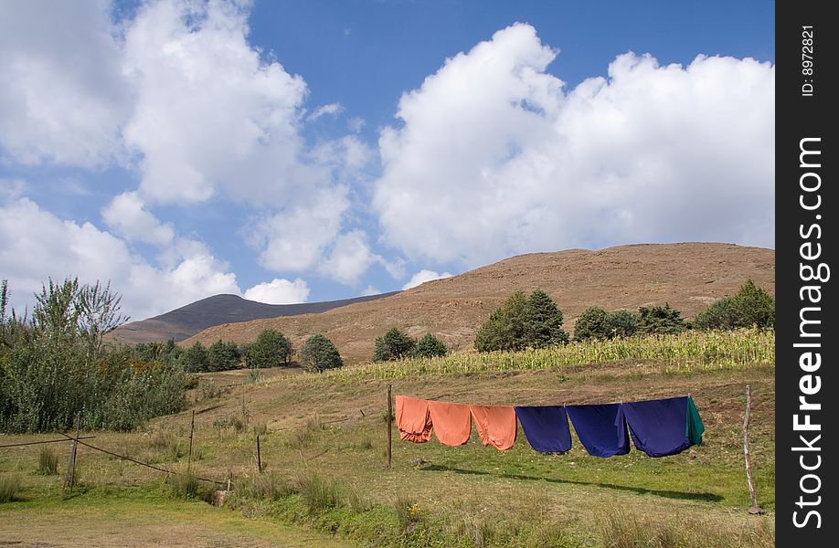 Orange and blue sheets on a clothesline in a rural setting with a maize field, trees and clouds in the background. Orange and blue sheets on a clothesline in a rural setting with a maize field, trees and clouds in the background