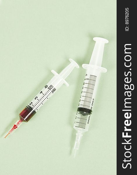 Two syringes on green background, one syringe filled with blood
