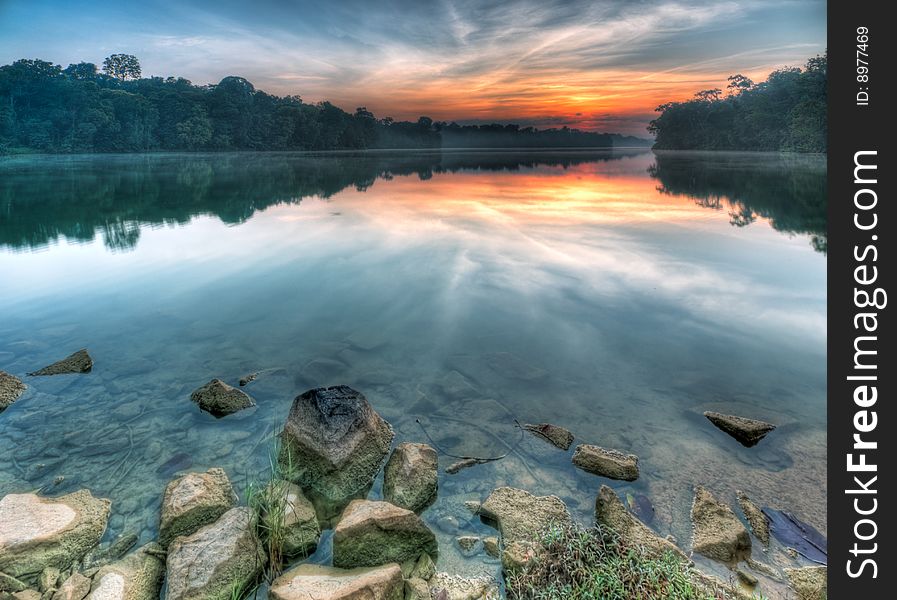 Sun below the ridge at dawn as seen from the rocky shores of a lake