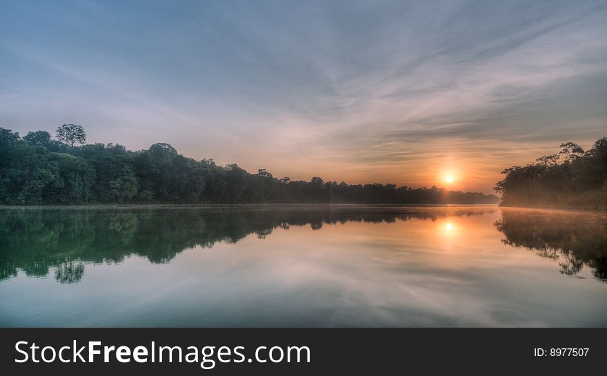 Sun crossing ridge at sunrise over a still lake