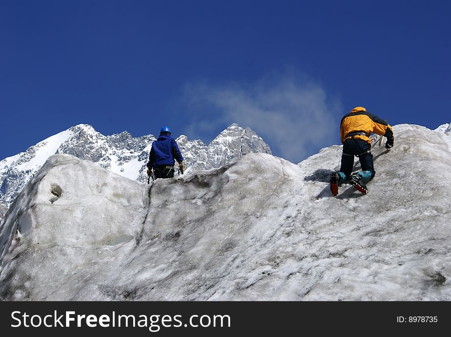 Two climbers practice on an ice wall on a background mountains. Two climbers practice on an ice wall on a background mountains