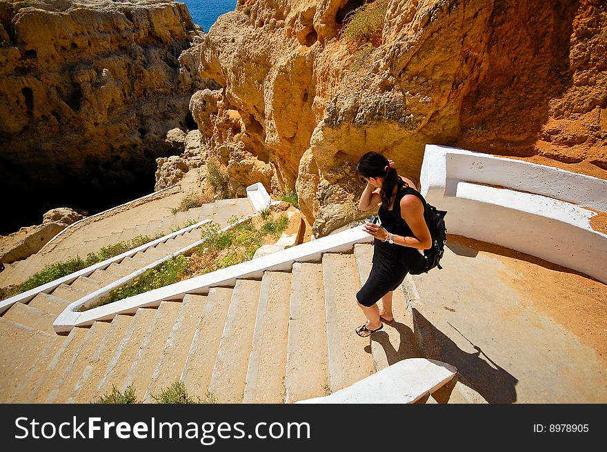 Woman in black take the stairs down to the cave formation at the Algarve coast. Woman in black take the stairs down to the cave formation at the Algarve coast.