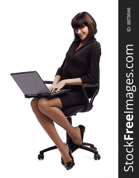 Flirting brunette woman in dark dress sitting in the office chair and holding laptop over white background